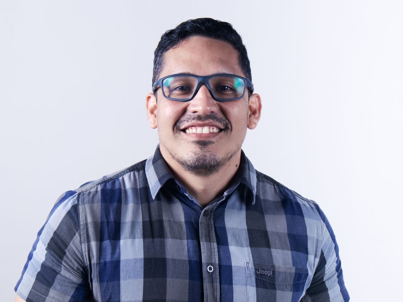 Casual portrait of a smiling man wearing glasses and a plaid shirt.